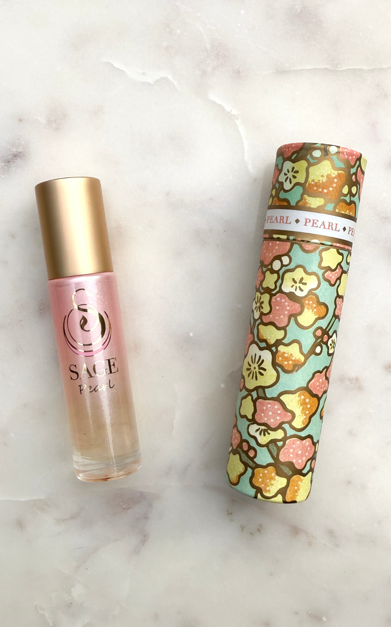 Perfume Roller bottle with a gold cap and pink body, Japanese washi paper box with a floral pattern, on a marble surface.