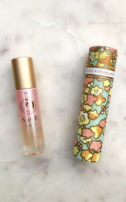 Perfume Roller bottle with a gold cap and pink body, Japanese washi paper box with a floral pattern, on a marble surface.